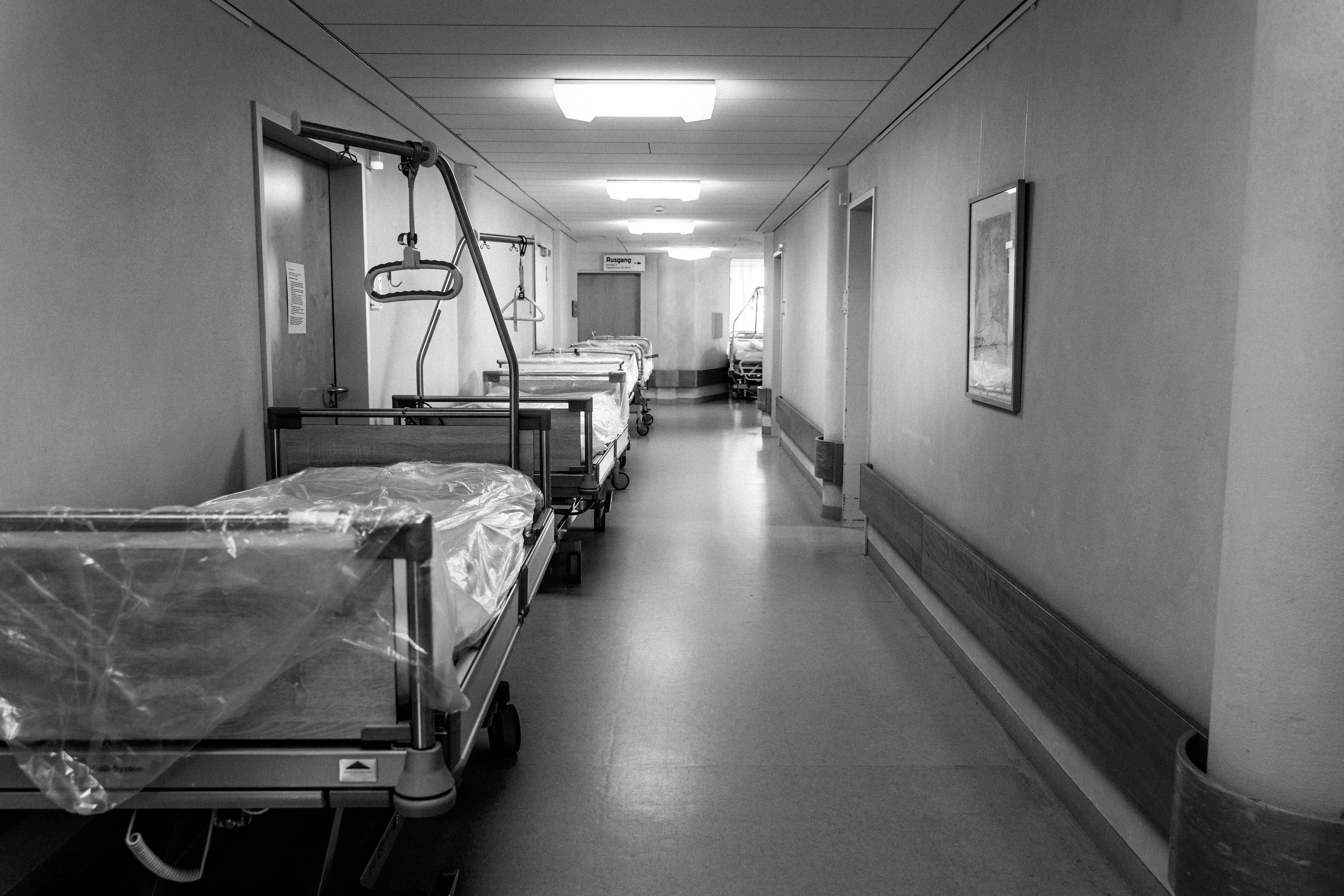 Black-and-white hospital corridor with empty patient beds